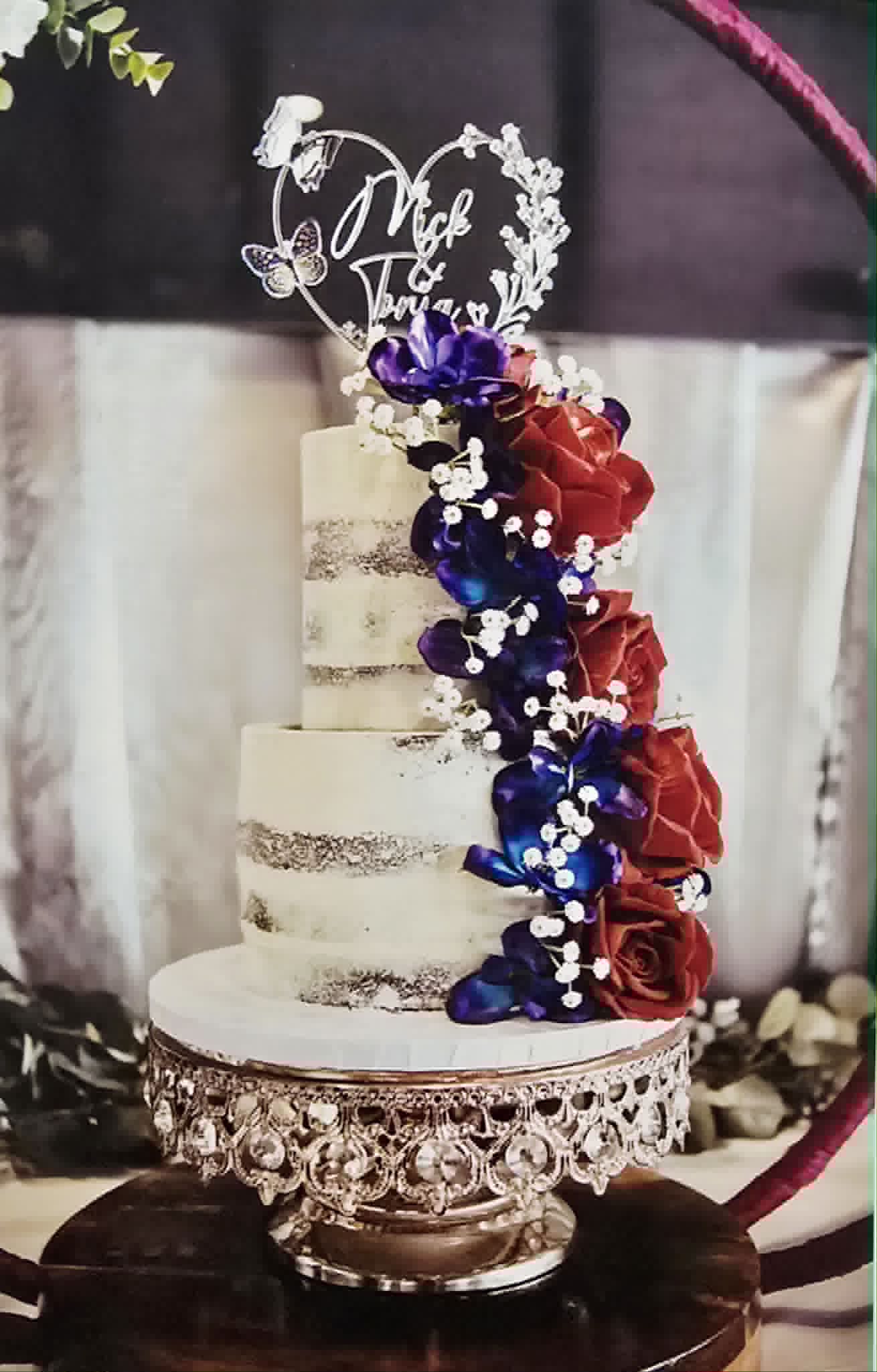 2 tier semi naked wedding cake with red and purple flowers.