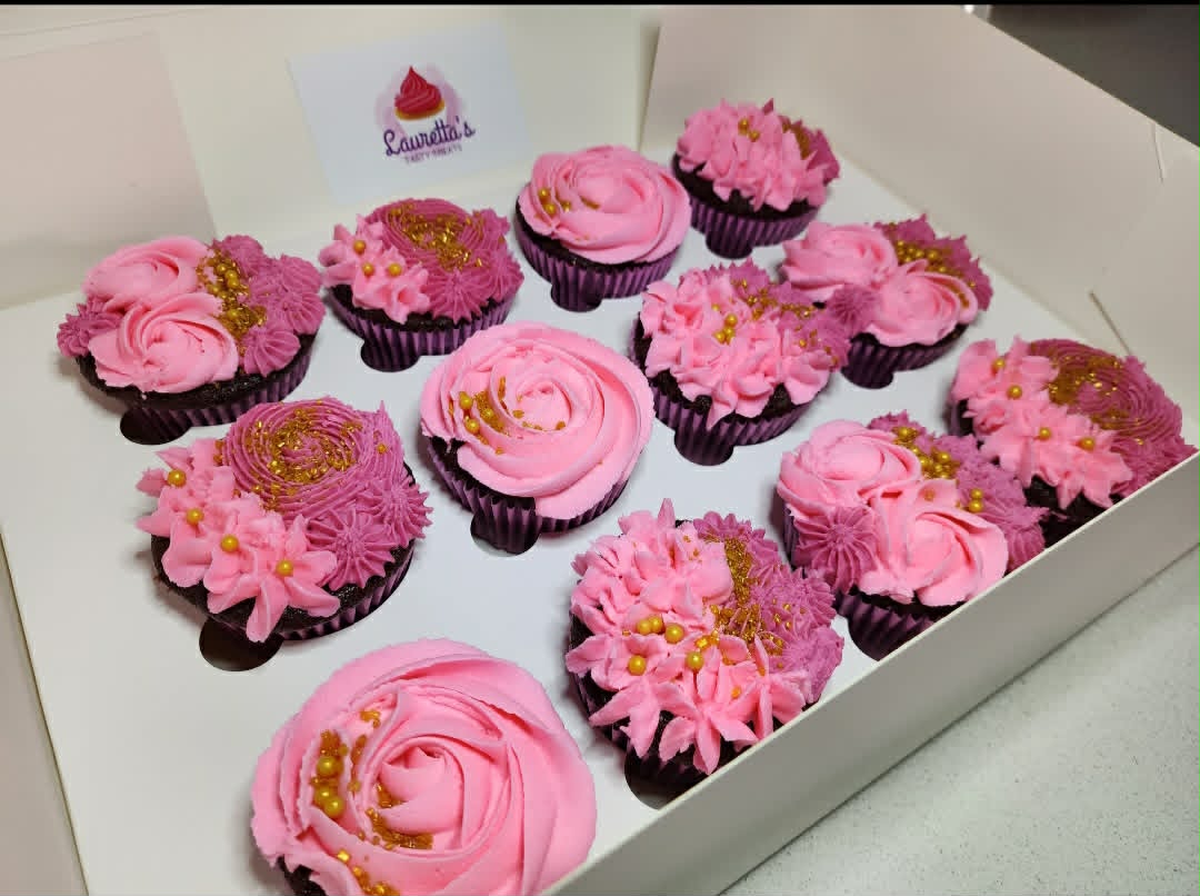 Box of cupcakes with pink frosting and gold decorations.