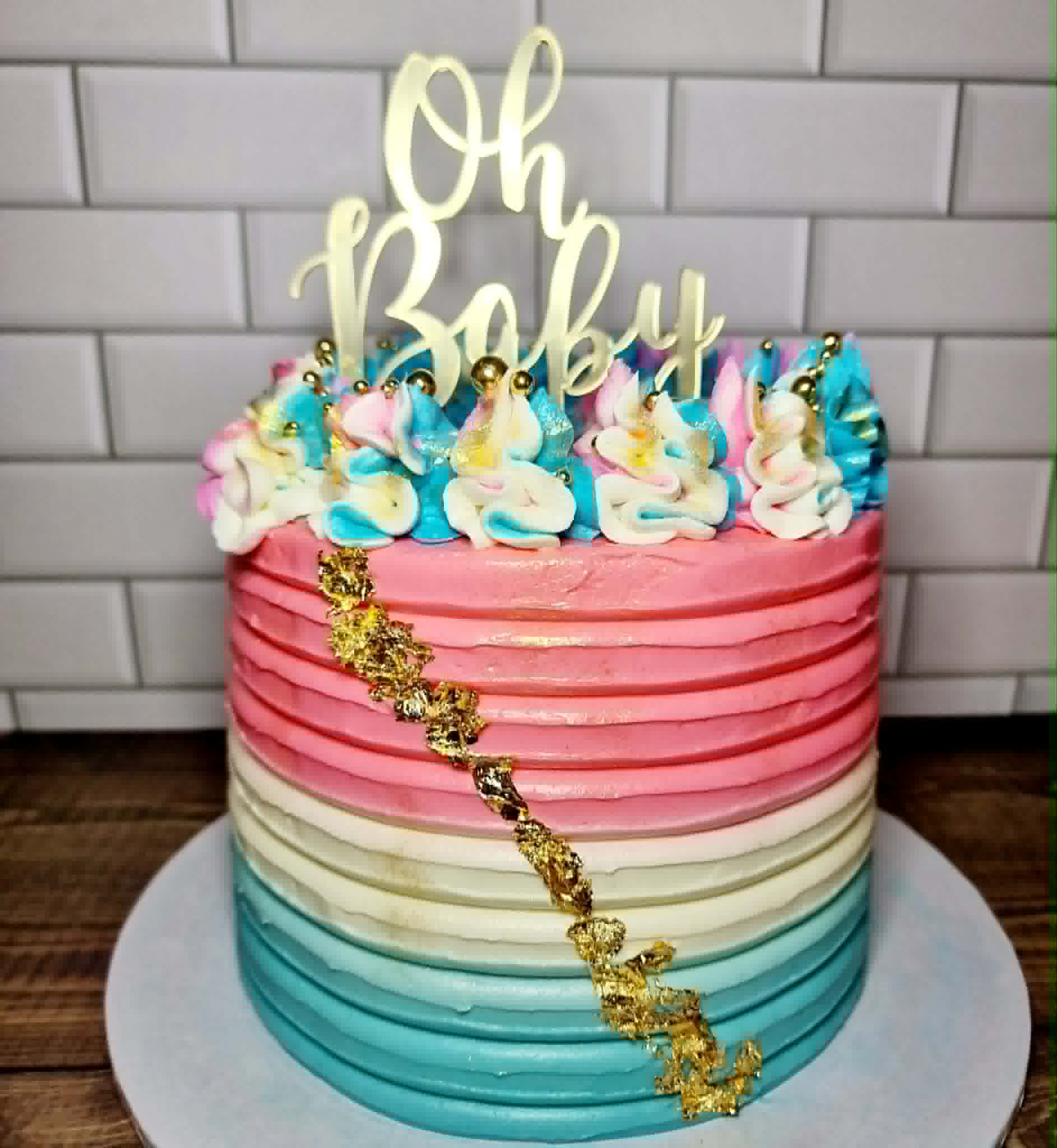 Colorful baby shower cake with 'Oh Baby' topper on a white tiled wall background