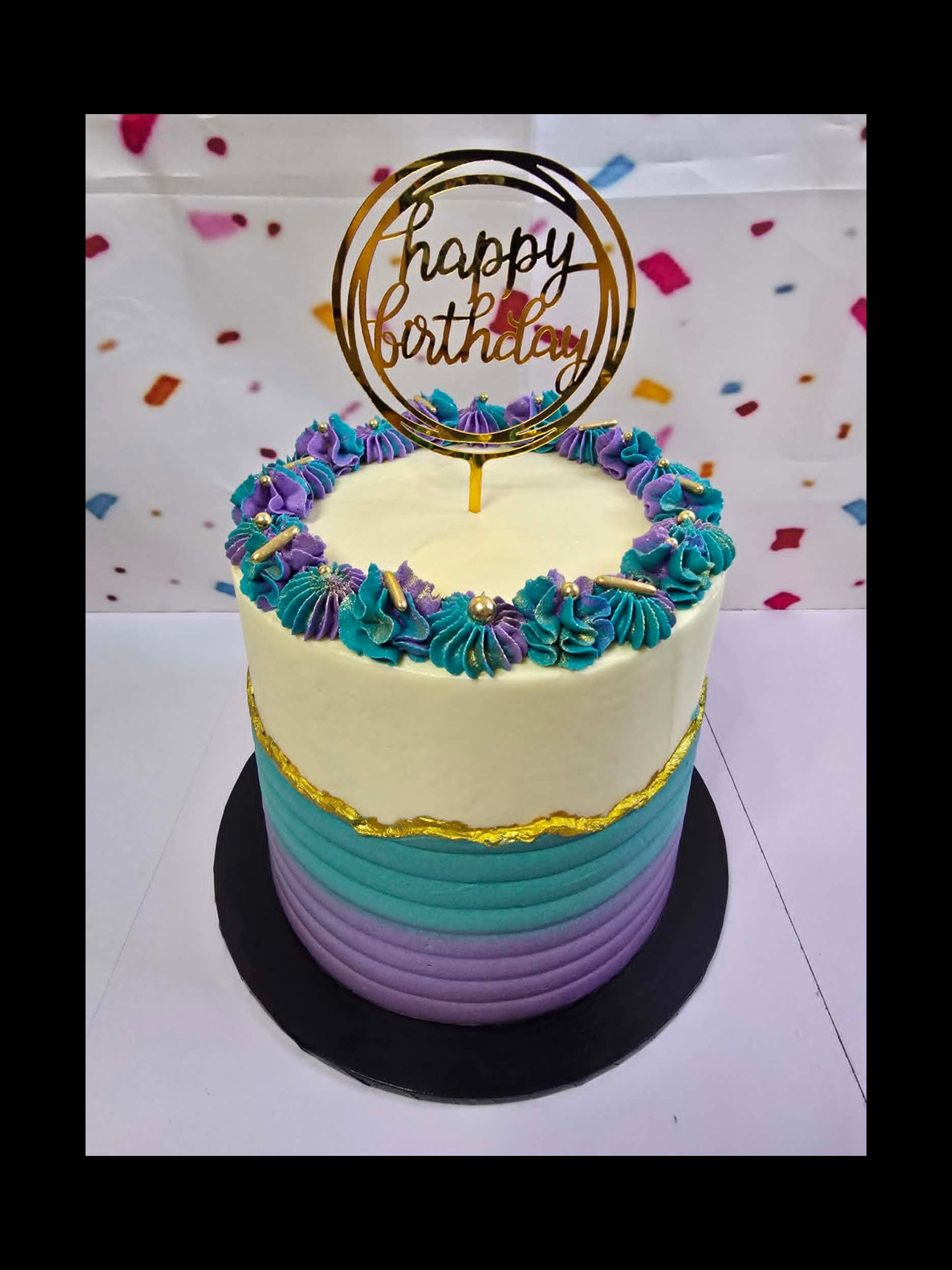 4 layer birthday cake with colourful frosting and 'Happy Birthday' topper on a white background.